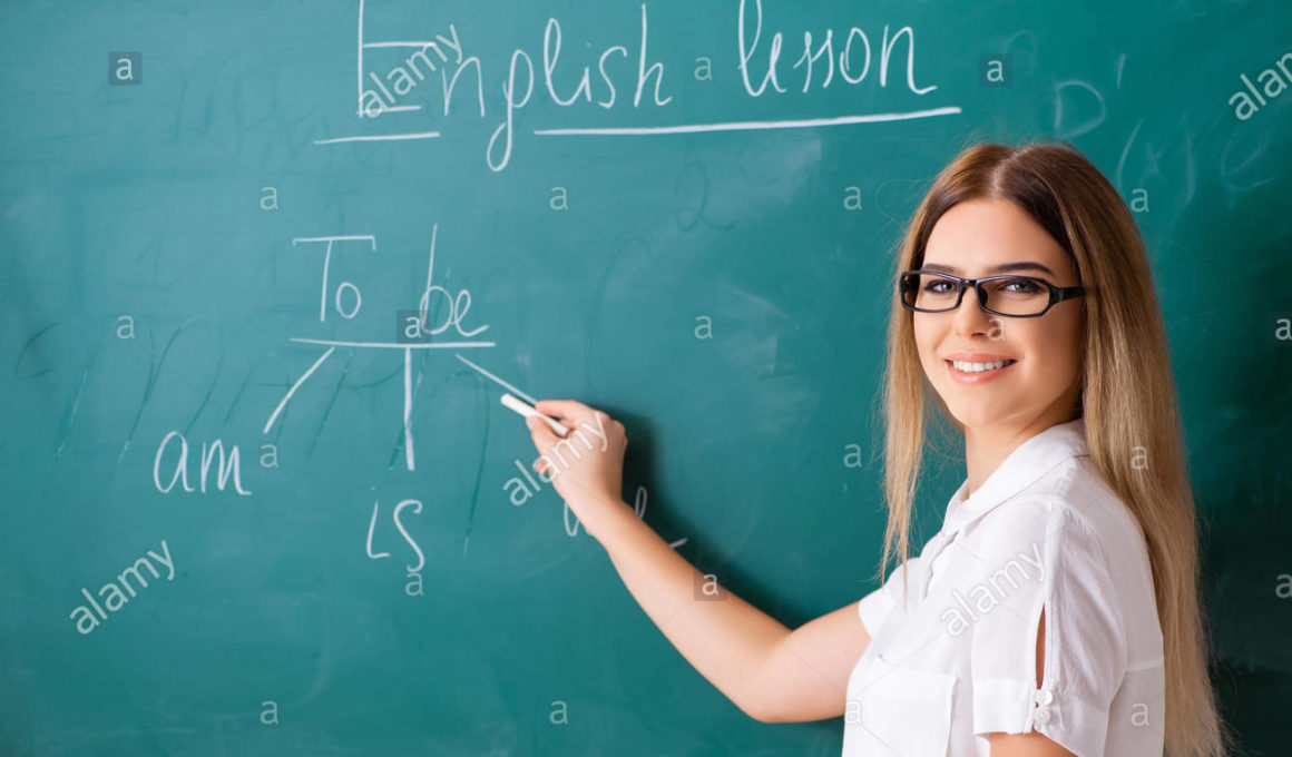 young female english language teacher standing in front of the blackboard RBM9DP
